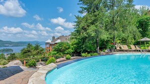 A swimming pool with lounge chairs, surrounded by greenery and a view of a lake and mountains. - Tremblant Prestige - Equinoxe 140-1 (Mont-Tremblant)