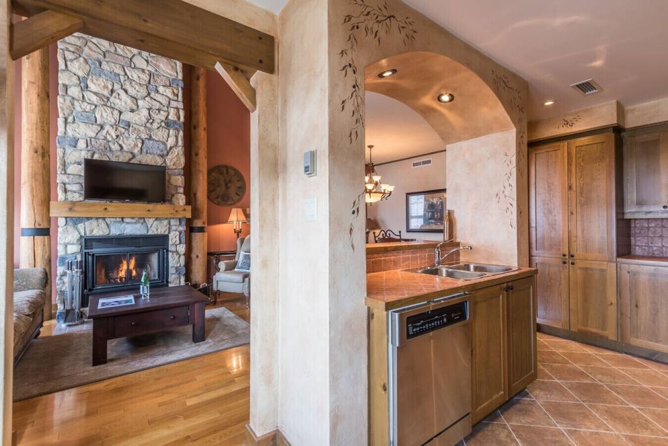 A modern kitchen with a stone fireplace, wooden cabinets, and a dishwasher.