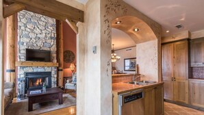 A modern kitchen with a stone fireplace, wooden cabinets, and a dishwasher. - Tremblant Prestige - Equinoxe 140-1 (Mont-Tremblant)