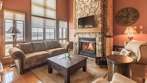 A cozy living room with a stone fireplace, a sofa, a coffee table, and a chair. - Tremblant Prestige - Equinoxe 140-1 (Mont-Tremblant)