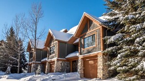 A large, multi-story log cabin with stone foundations and wooden trim, surrounded by snow-covered trees and a clear sky. - Tremblant Prestige - Equinoxe 140-1 (Mont-Tremblant)