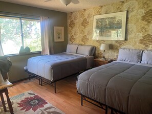 A bedroom with two beds, a window with curtains, a framed picture on the wall, and a wooden floor.