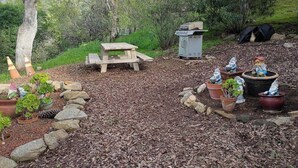 En plats för picknick med ett träbord och bänkar, omgiven av krukväxter och trädgårdstomtar.