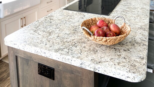 Una cocina con encimeras de granito, horno empotrado y una cesta de manzanas.