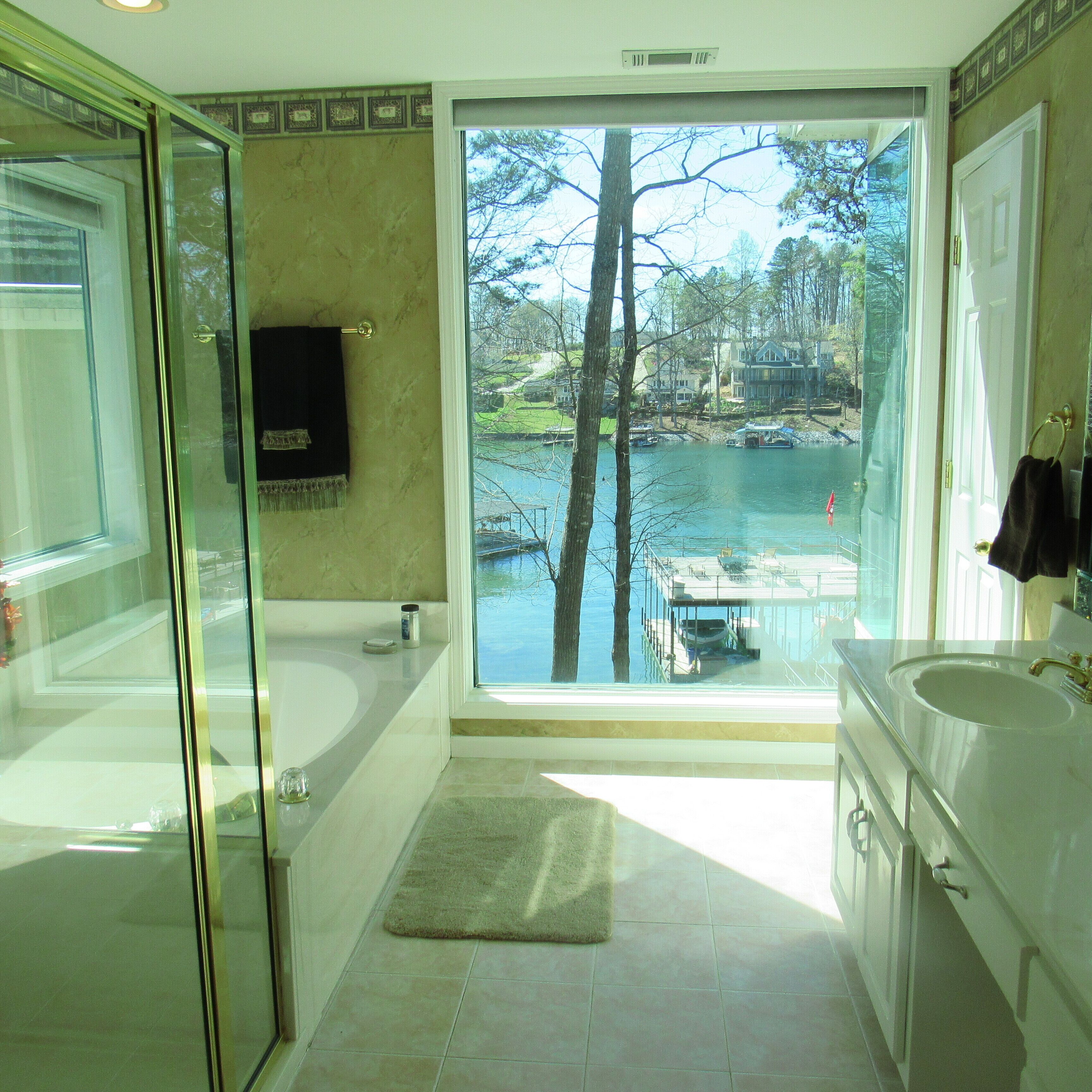 Une salle de bain dotée d’une porte de douche en verre, d’une baignoire, d’un lavabo et d’une grande fenêtre donnant sur un lac et un quai.