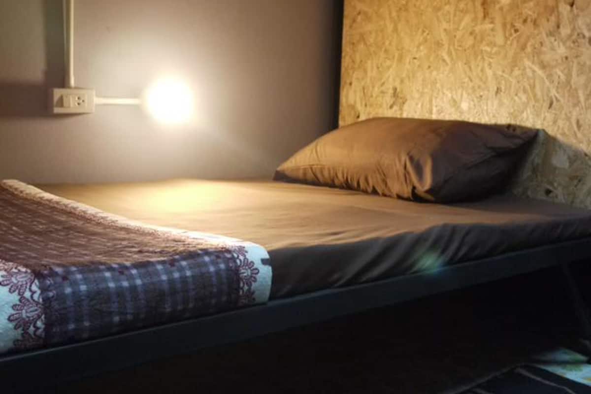 A single bed with a headboard made of wood, a bedside lamp, and a patterned bedspread.