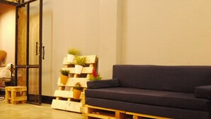 A room with a dark-colored sofa, wooden pallets, and a wall-mounted plant shelf. - Asleep Hostel (Kanchanaburi)