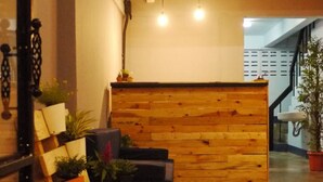 A reception area with a wooden reception desk, a staircase, and potted plants. - Asleep Hostel (Kanchanaburi)