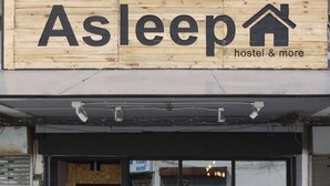 A hostel named Asleep with a wooden signboard, a glass door entrance, and outdoor seating. - Asleep Hostel (Kanchanaburi)