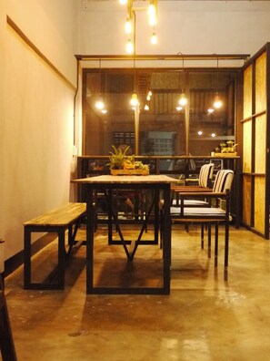 Un comedor acogedor con una mesa de madera y bancos, una planta en maceta sobre la mesa, y lámparas colgantes.