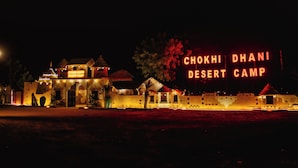 A desert camp with illuminated signage reading 'CHOKHI DHANI DESERT CAMP'. - Chokhi Dhani Desert Camp (Jaisalmer)