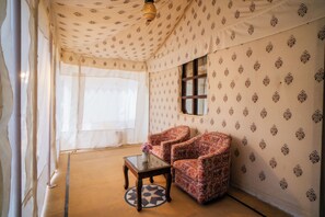 Una habitación con papel tapiz estampado, una ventana, una silla, una mesa y una lámpara de pie.