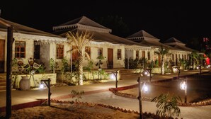 A row of traditional-style buildings with a paved walkway and palm trees. - Chokhi Dhani Desert Camp (Jaisalmer)