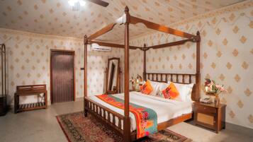 A four-poster bed with a colorful bedspread, a wooden nightstand with a vase, and a patterned wall.