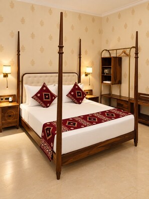 A four-poster bed with a wooden frame, two matching pillows, and a red patterned bedspread. There are two bedside tables with lamps, a wooden nightstand, and a wooden wardrobe with a mirror.