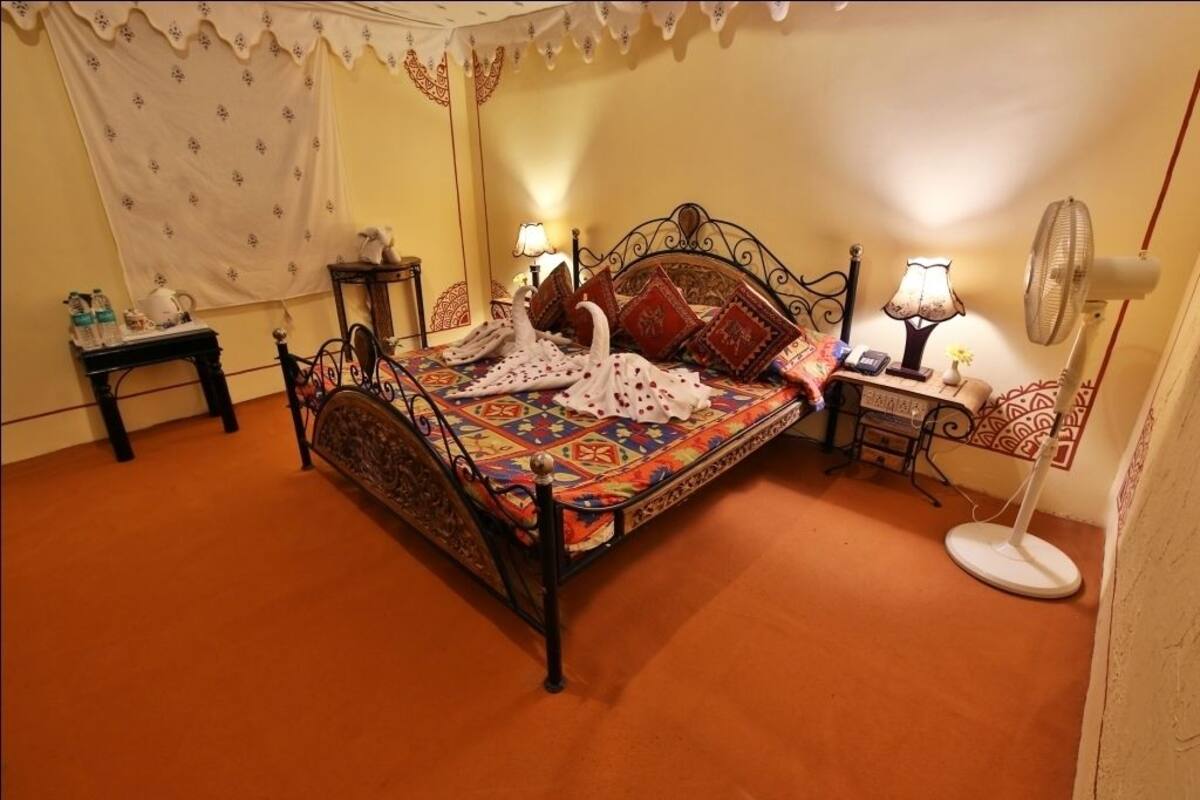 Ein Schlafzimmer mit einem Bett, zwei Nachttischen, einem Wandventilator und einem Vorhang.