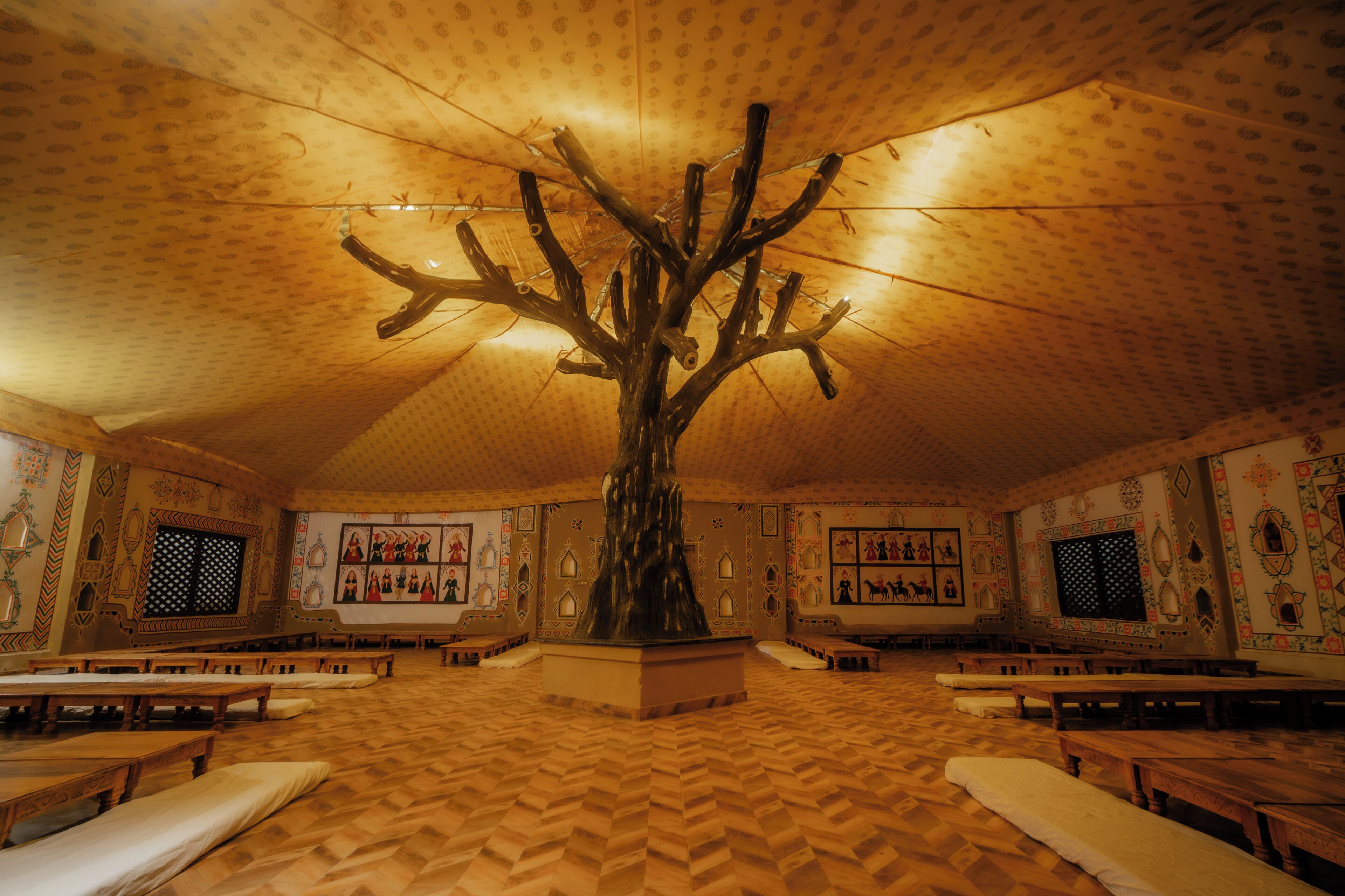 A room with a large tree sculpture at the center, wooden benches, patterned walls, and a herringbone floor.
