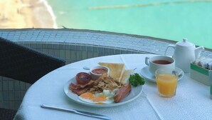 A breakfast table with eggs, bacon, toast, and juice, overlooking a beach and ocean. - The Warwick (Cheung Chau)
