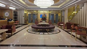 A spacious lobby with a central round seating area, a large chandelier, and a reception desk. - Grand Continental Hotel  (Prayagraj)