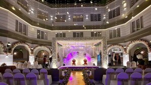 A multi-level indoor venue with a central stage, rows of white chairs, and a decorative floral pathway. - Grand Continental Hotel  (Prayagraj)