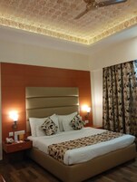 Una habitación de hotel con una cama grande, dos mesitas de noche, un ventilador de techo y una ventana con cortinas.