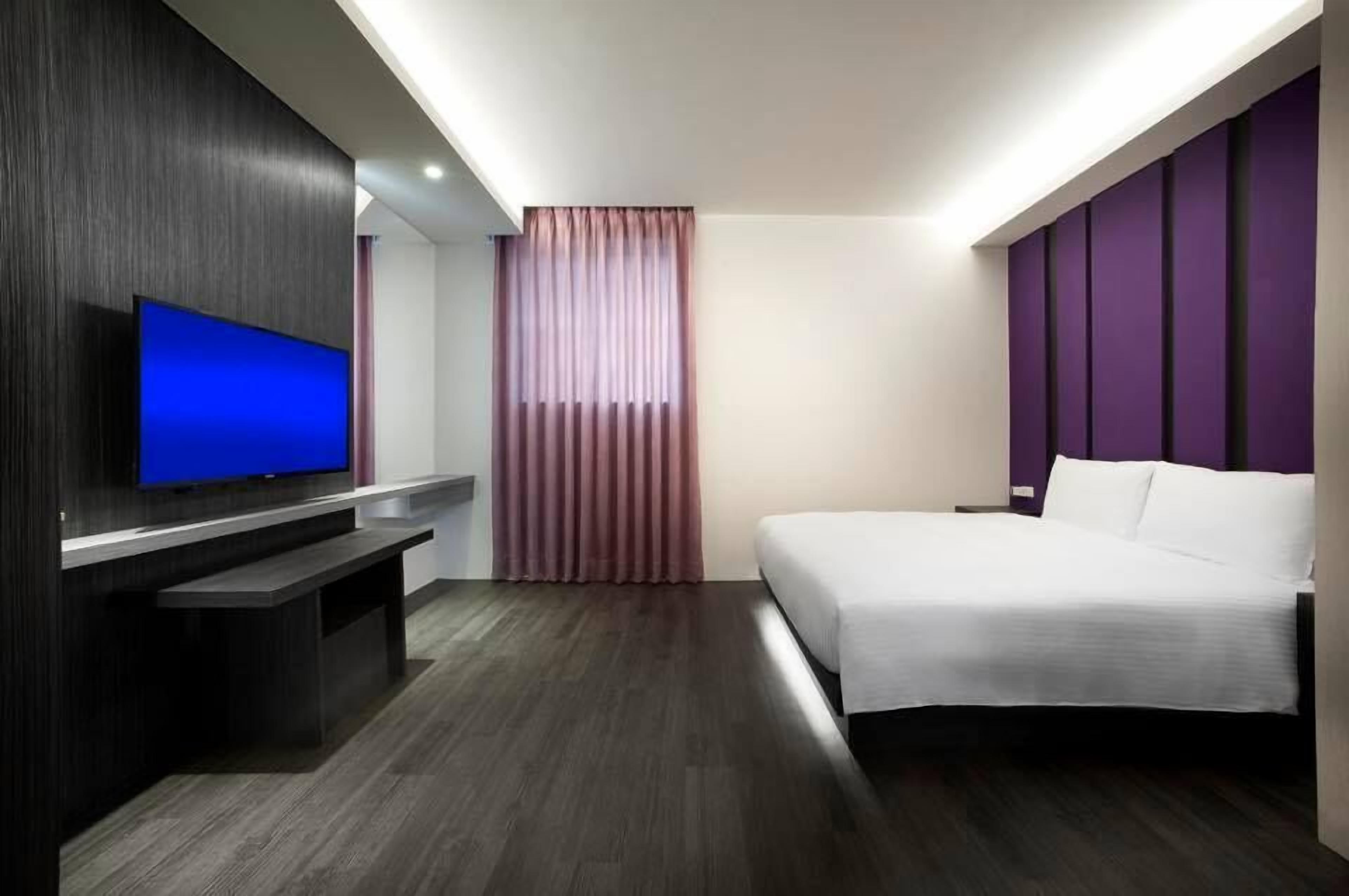 Una habitación de hotel moderna con un televisor de pantalla plana, una cama y un ventanal con cortinas.