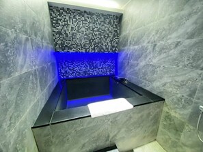 Une salle de bain moderne avec une baignoire noire, des murs carrelés et un éclairage bleu.