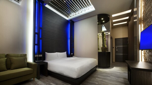 Una habitación de hotel moderna con una cama grande, un sofá verde, un escritorio y una lámpara en el techo.