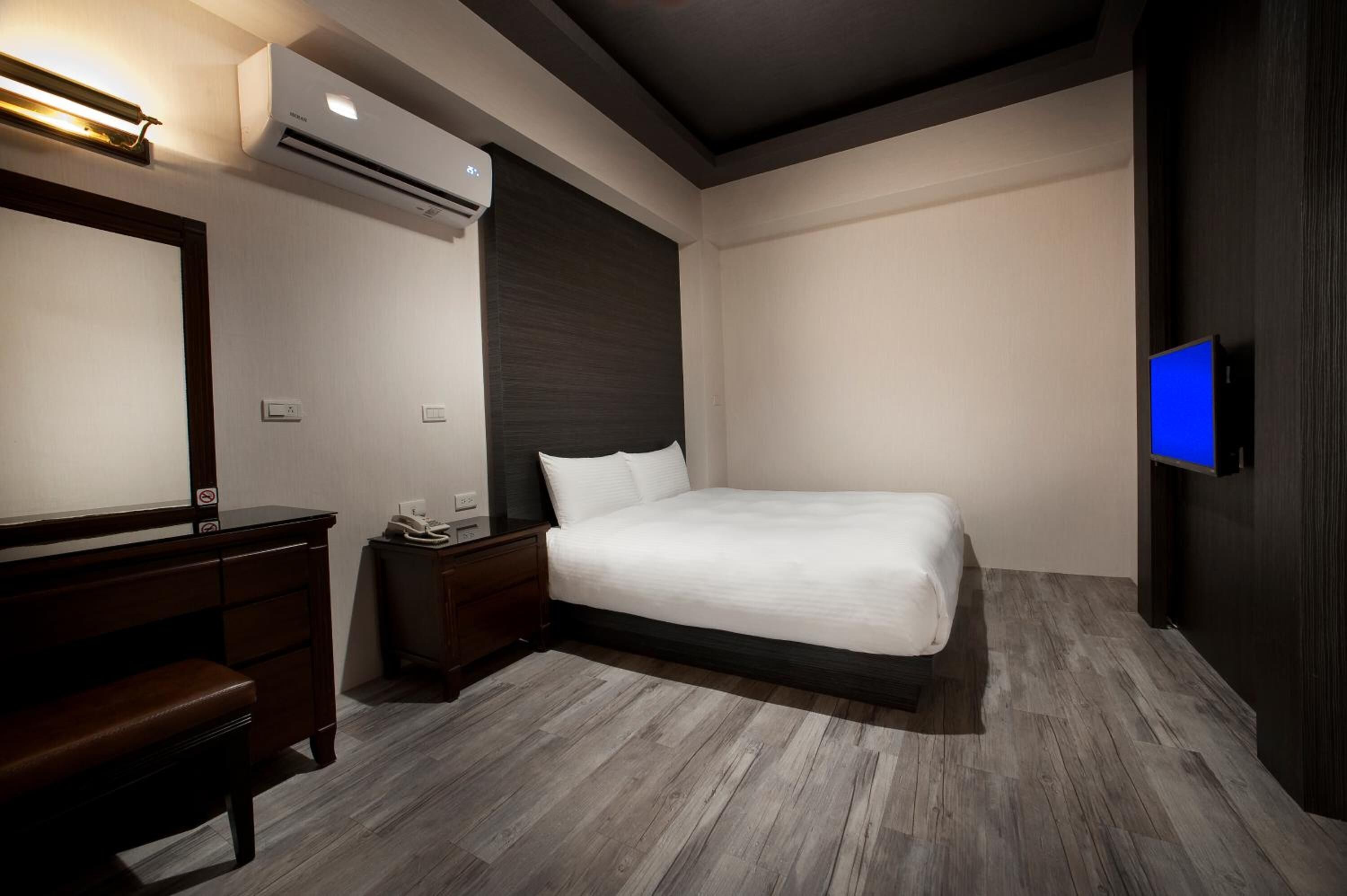 Habitación de hotel con cama, escritorio, silla, televisor y aire acondicionado.