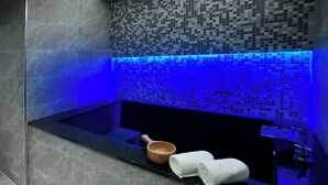 Un baño moderno con una bañera negra, un revestimiento de mosaicos y luz azul.