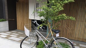 Una bicicleta estacionada frente a un edificio con cerca de bambú y un letrero que dice 'Hotel Nagano Kyoto'.