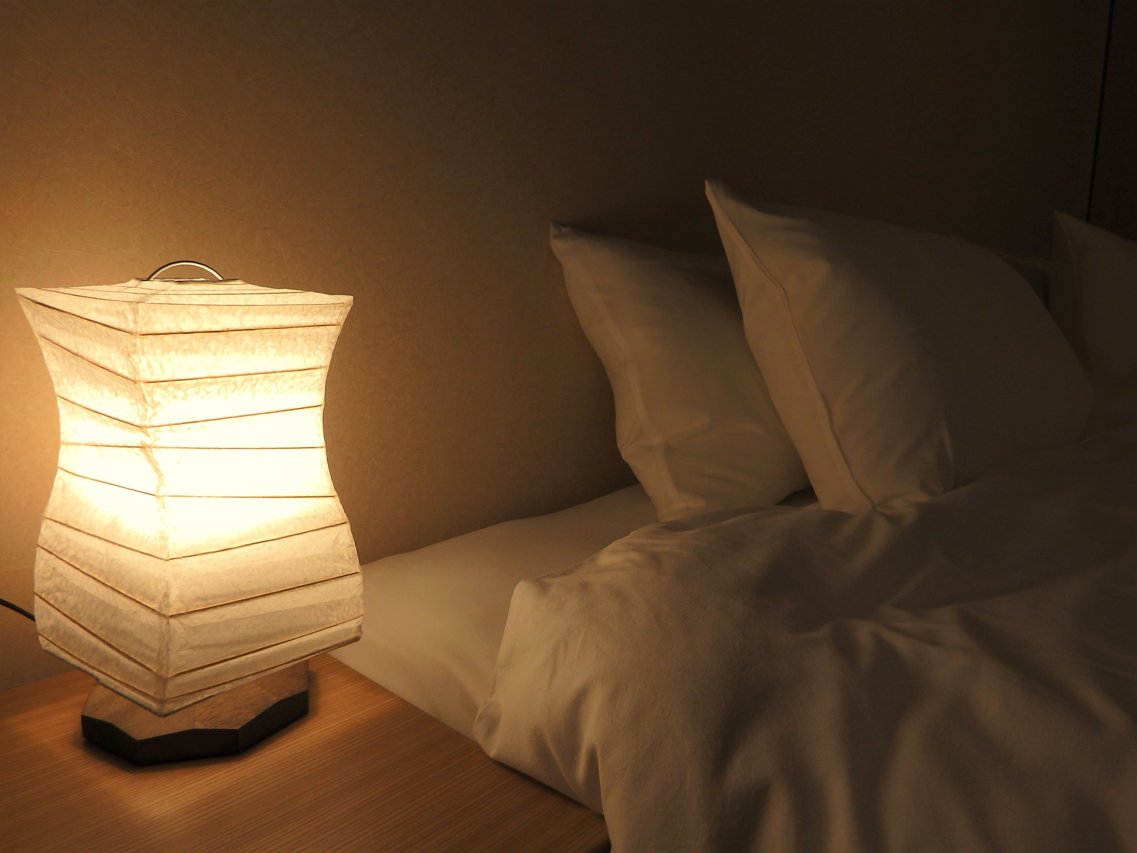 Un comodino con una lampada a paralume in stile lanterna accesa, accanto a un letto con lenzuola bianche.