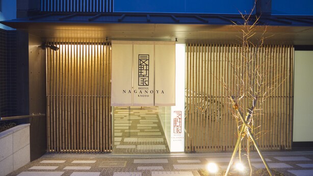Exterior del Hotel Nagano A en Kioto, con una fachada moderna que presenta paneles verticales de bambú y un letrero de entrada llamativo.