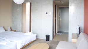 Habitación de hotel moderna con una cama grande, una mesita de noche de madera, una lámpara blanca, un cubo de basura pequeño y un televisor.