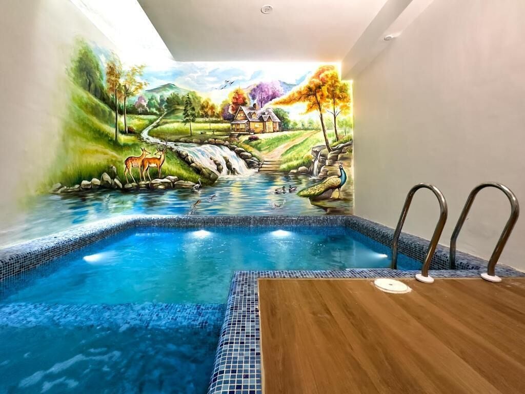 Una piscina con un mural que representa un paisaje, incluyendo una cascada, ciervos y una casa.