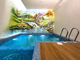 Una piscina con un mural que representa un paisaje, incluyendo una cascada, ciervos y una casa.