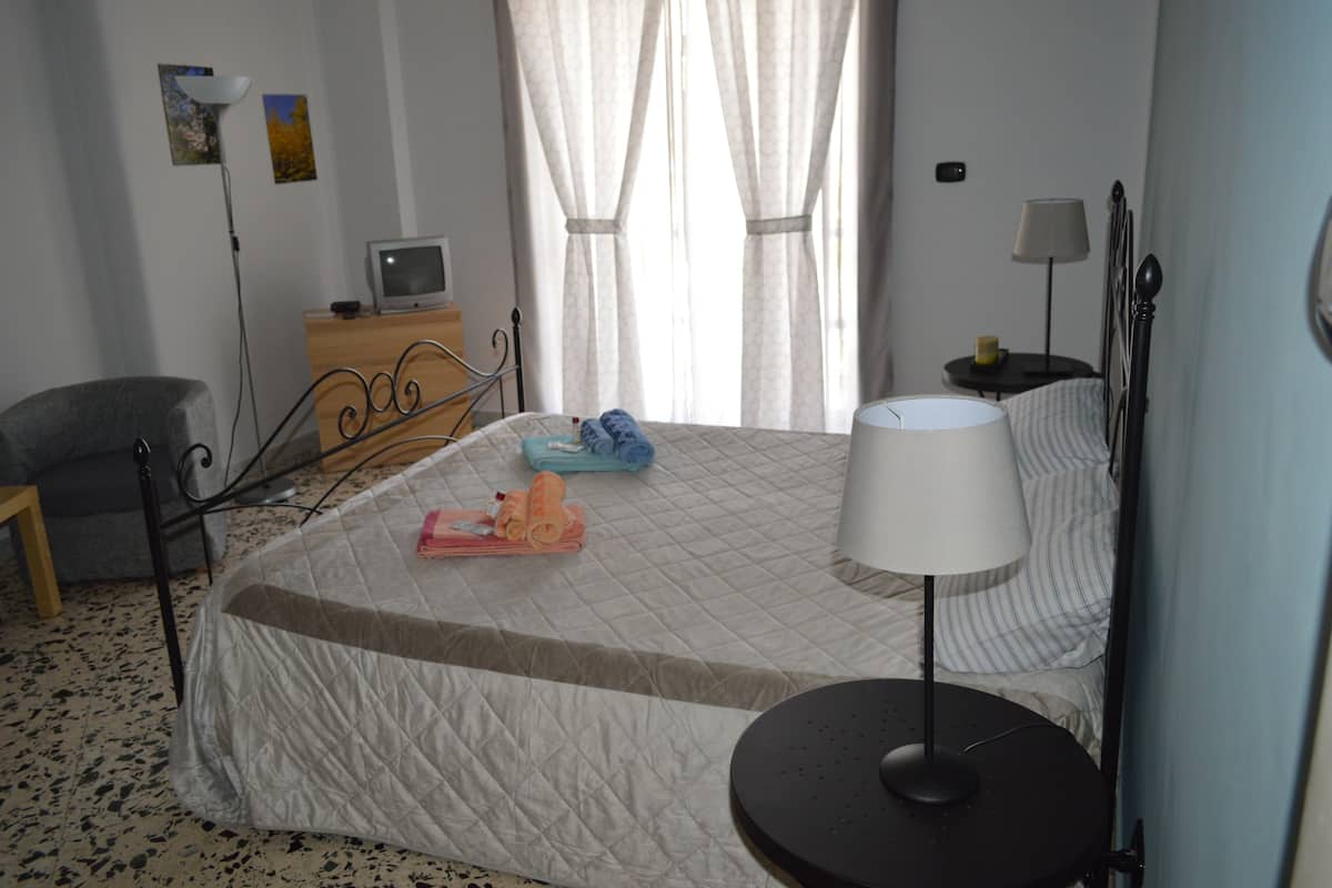 A bedroom with a bed, bedside table, lamp, chair, and a television on a dresser.