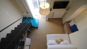 A bedroom with a bed, a staircase, a TV, and a window.
