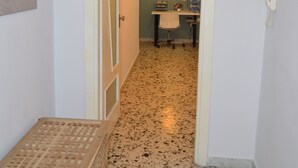 A hallway with a door leading to a room with a desk and chair, a telephone, and a wall-mounted light fixture.