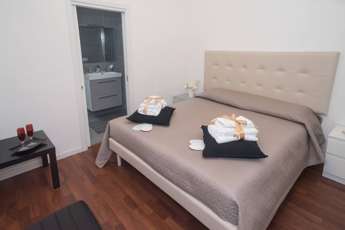Habitación de hotel ordenada con cama, mesita de noche y una pequeña mesa con vasos.