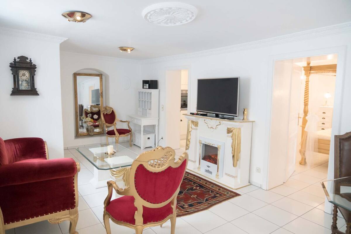 Ein geräumiges Wohnzimmer mit Kamin, Fernseher und einem roten Sessel.