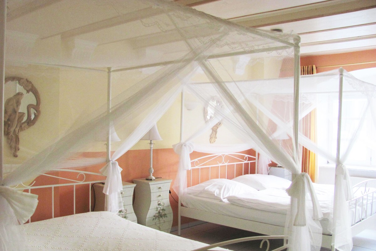 Una habitación con dos camas, cada una con dosel, mesita de noche y lámpara de pared.