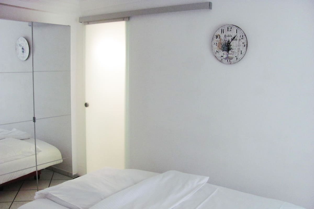 Ein Hotelzimmer mit einem Einzelbett, einer Wanduhr und einer Tür zu einem anderen Raum.