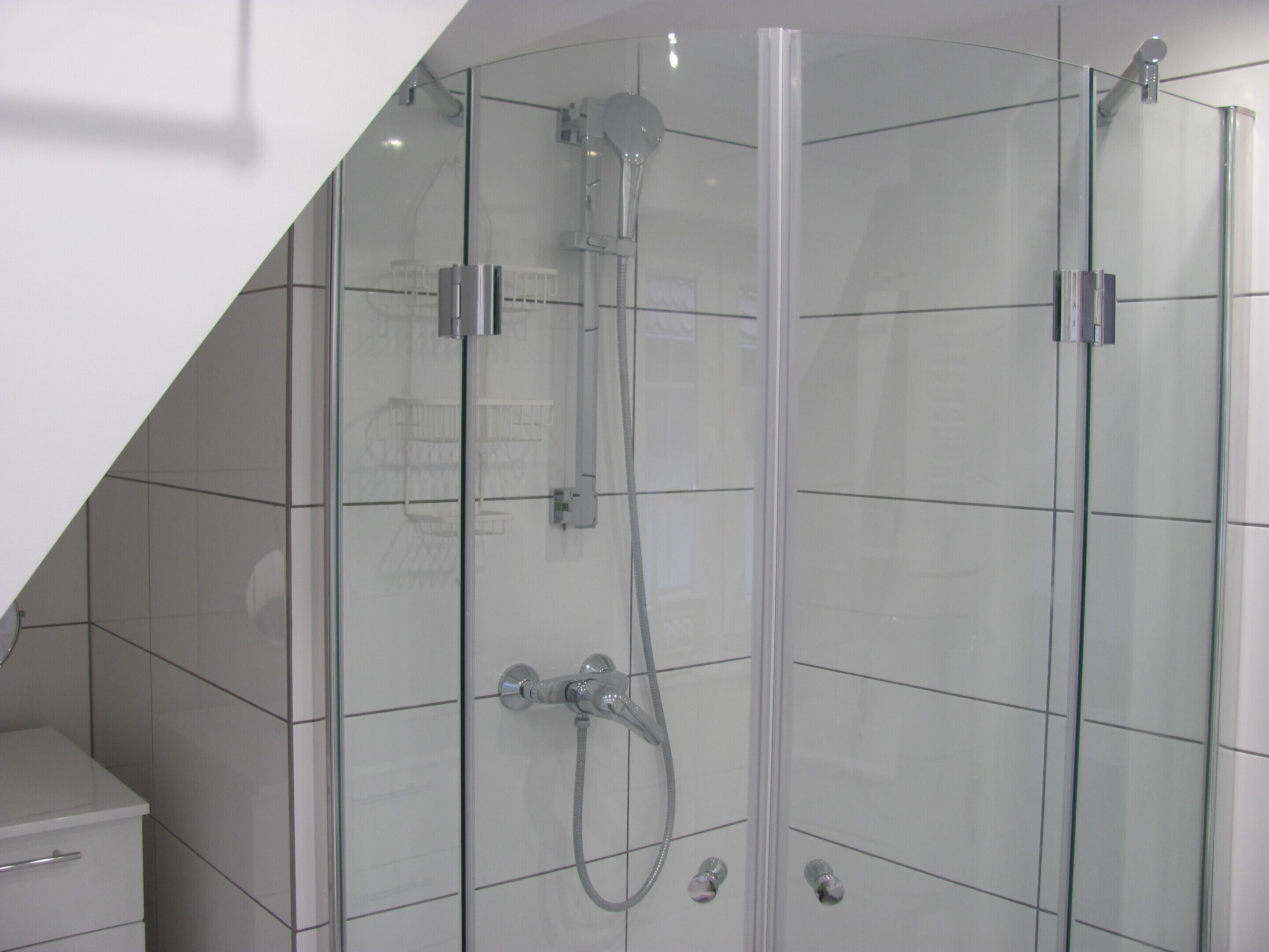 A glass-enclosed shower stall with a handheld showerhead and a wall-mounted faucet.