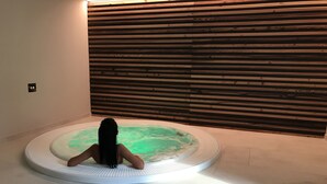 A person sitting in a circular hot tub with a wooden panel wall behind them. - Dolomeet Boutique Hotel (Pinzolo)