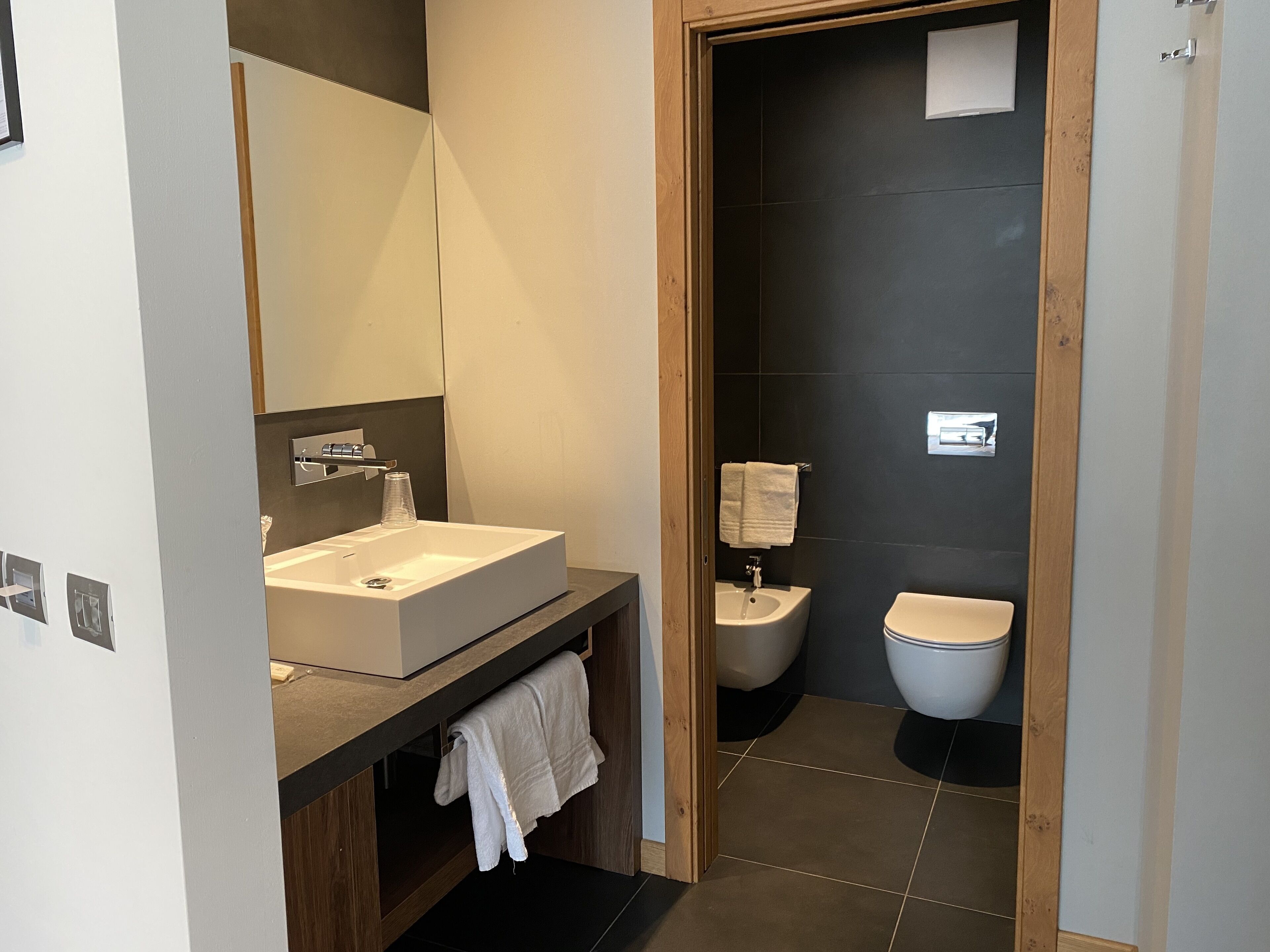 Un baño moderno con un lavamanos grande, espejo y paredes de azulejos oscuros.