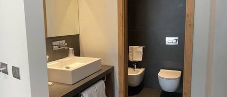 Un baño moderno con un lavamanos grande, espejo y paredes de azulejos oscuros.