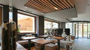 A modern interior with wooden tables and benches, large windows, and a view of the outside. - Dolomeet Boutique Hotel (Pinzolo)