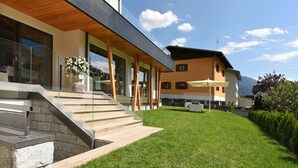 A modern building with a wooden deck, a stone staircase, and a well-maintained lawn. - Dolomeet Boutique Hotel (Pinzolo)