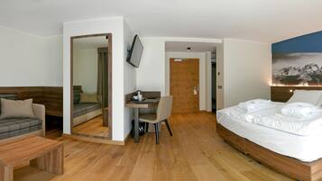 A modern hotel room with a bed, a sofa, a desk, and a mirror.